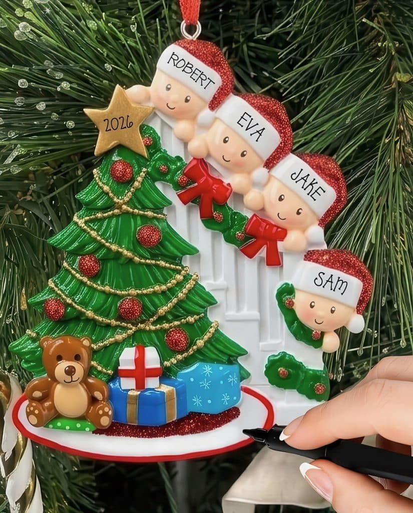 Decorative Christmas ornament: four children’s heads in Santa hats around a festive tree with gifts and a teddy bear, held by a hand with a pen nearby.